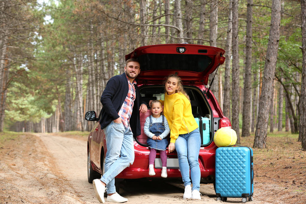 Happy young family near car trunk loaded with suitcases outdoors - Valokuva, kuva