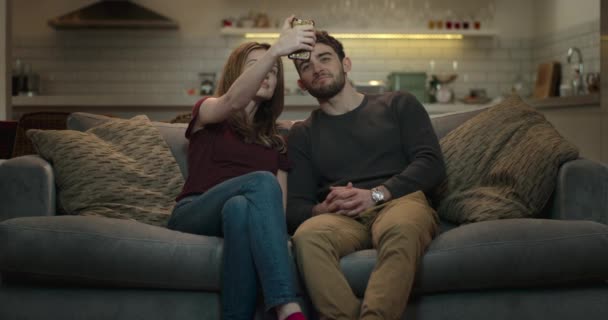 Ein Paar, das auf einem Sofa sitzt, teilt einen Moment, indem es ein Selfie auf seinem Smartphone macht und es an seine Freunde schickt.. - Filmmaterial, Video