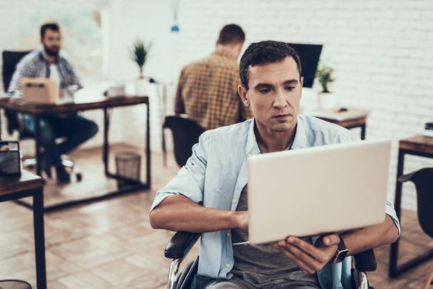 Disabled Man on Wheelchair with Laptop in Office. Disabled Young Man. Man on Wheelchair. Recovery and Healthcare Concepts. Teamwork in Office. Young Worker. Sitting Man. Worker with Laptop. - Фото, изображение