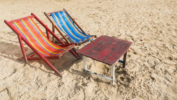 Punainen ja sininen rantatuoli punaisella puupöydällä rannalla. Kesäkonsepti lämpimässä auringonvalossa
 - Valokuva, kuva