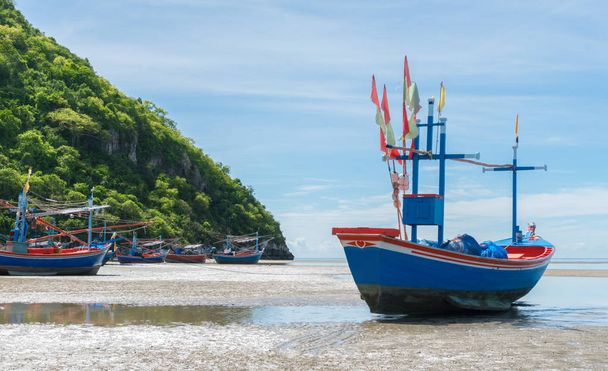 Barco de pesca azul en la arena del mar con colina verde y otro barco de pescador en la playa de Khao Kalok Tailandia. Barco de pescadores en arena gris con árbol
 - Foto, imagen