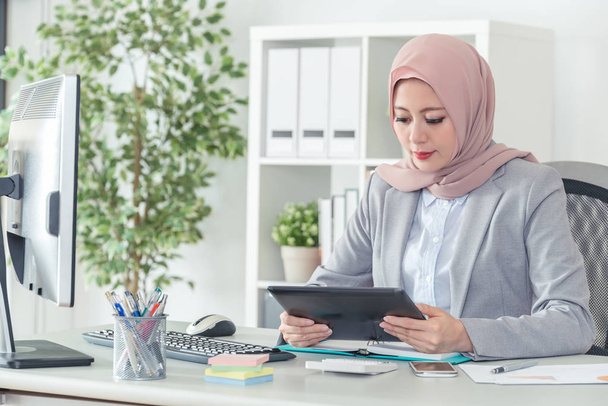 Muslim female employee looking at the tablet and thinking for the next plan.Serious businesswoman busy working on digital pad at work. Beautiful office lady being concentrated. - Foto, immagini