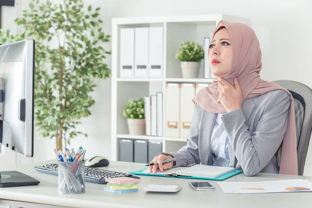 a muslim office lady is confused and thinking about the solution with her chin on her hand. Thinking office worker day dreaming looking up with a sad face in work place. - Foto, Imagem