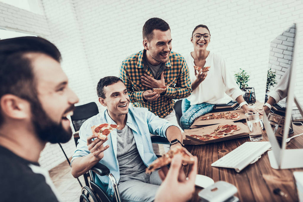 Young People Have Lunch with Pizza in Office. Teamwork in Office. Young Worker. Sitting Man. Box with Pizza. Young Girl in Glasses. Young Worker. Manager on Break. Man on Wheelchair. - Φωτογραφία, εικόνα
