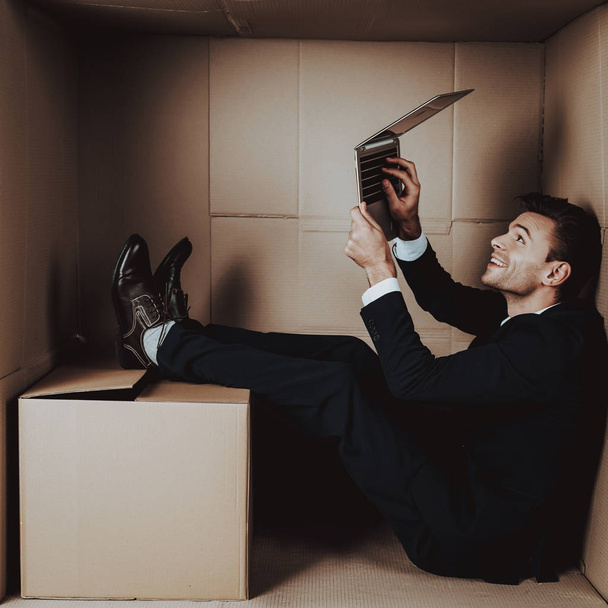 Young Businessman with Laptop in Cardboard Box. Young Man in Suit. Life in Little Cardboard Box. Uncomfortable Life. Personal Spase Concepts. Using Digital Device. Young Introvert. - Foto, Imagen
