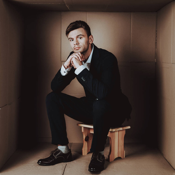 Young Businessman in Black Suit in Cardboard Box. Young Man in Suit. Life in Little Cardboard Box. Uncomfortable Life. Personal Spase Concept. Uncomfortable House Concept. Young Introvert. - 写真・画像