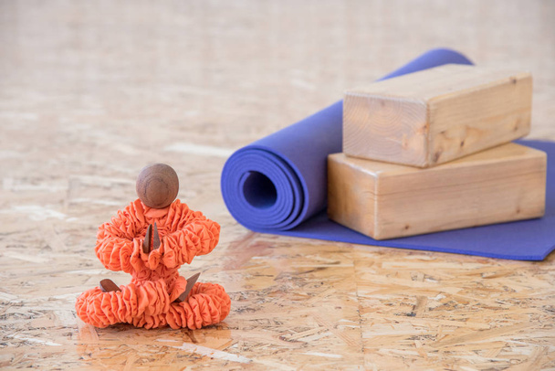 Figurine in orange clothes sitting in a yoga pose with a purple mat for exercise and meditation - Photo, Image