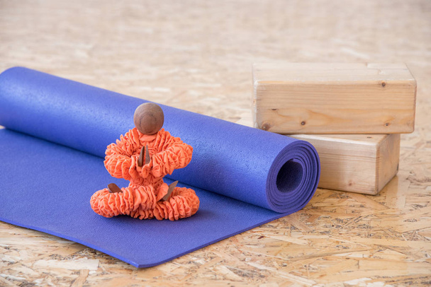 Figurka v oranžové oblečení sedí v jóga představuje s fialovým podložka pro cvičení a meditace - Fotografie, Obrázek