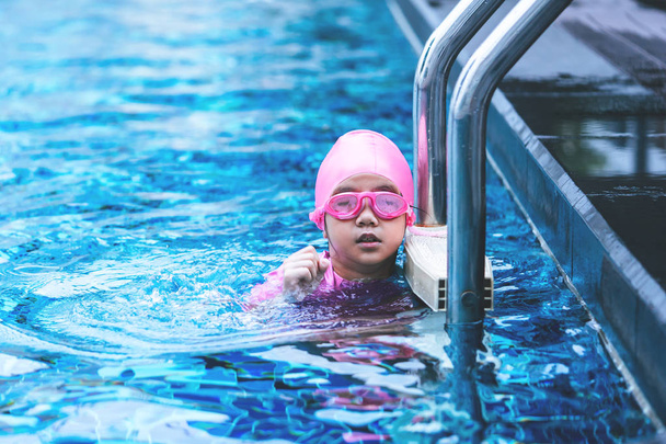 Klein aziatisch meisje is zwemmen met bril op de ladder - Foto, afbeelding