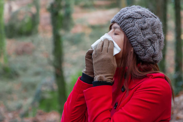 Mujer joven que sufre de un resfriado, gripe o alergias sonándose la nariz en un pañuelo de papel blanco durante el invierno
 - Foto, Imagen