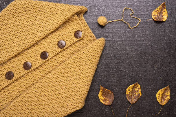Autumn composition with a yellow crocheted cardigan, dried leaves and a small ball of yarn on a black background. - Zdjęcie, obraz