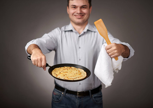 man posing with a pancake in a pan, white shirt and pants, gray background, shallow depth of field, sharp pancake and blurred face - Photo, Image