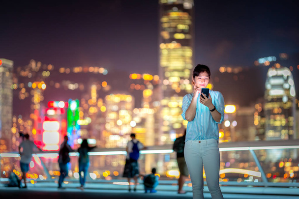 Mujer joven usando el teléfono inteligente en la calle de la ciudad de Hong Kong por la noche
 - Foto, imagen