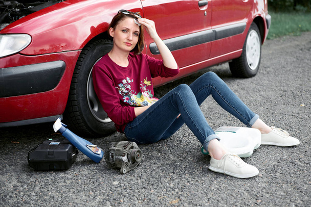kırık bir arabanın yakınında oturan ve onu orada yanında yardım arayan bir genç kızsın kötü parçalar, elektrik jeneratörü, araçları ve ilk yardım kiti - Fotoğraf, Görsel