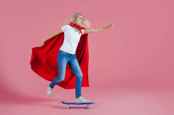 superhero on a skateboard. Funny young woman in the image of a superhero to the rescue - Photo, Image