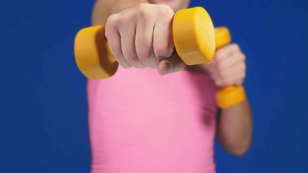A man in a pink T-shirt with a deep neckline is boxing dumbbells. focus on dumbbells, body blurry. copy space - Photo, Image