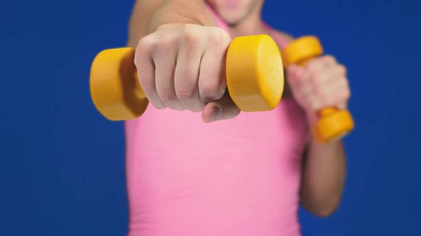 A man in a pink T-shirt with a deep neckline is boxing dumbbells. focus on dumbbells, body blurry. copy space - Photo, image