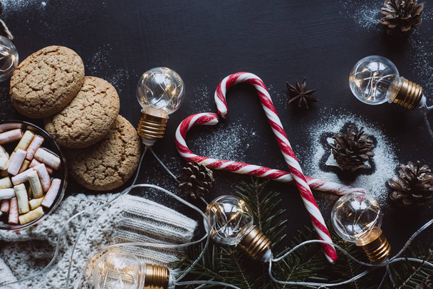 Christmas flat lay. Chocolate or cocoa with marshmallow, cookies, candy and the garland on a dark background. - Φωτογραφία, εικόνα