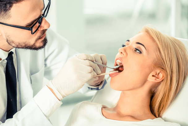 Young handsome dentist examining teeth of happy woman patient sitting on dentist chair in dental clinic. Dentistry care concept. - Foto, Imagem