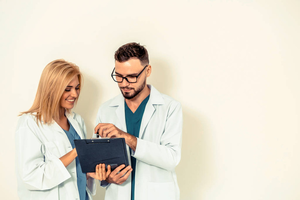 GP doctor looks at data in documents on clipboard while discussing with surgical doctor on white background. Medical service and healthcare concept. - Photo, image