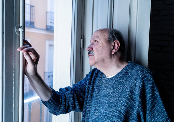 Senior man in his 60s feeling desperate sad looking throughout the balcony worried depressed thoughtful and lonely at home in Aging Depression Mental health Personal problems and Life style concept. - Photo, image