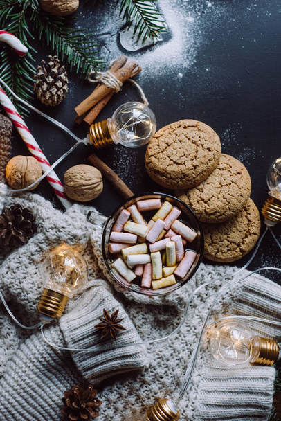Christmas flat lay. Chocolate or cocoa with marshmallow, cookies, candy and the garland on a dark background. - Φωτογραφία, εικόνα