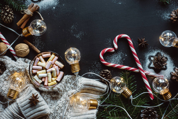 Christmas flat lay. Chocolate or cocoa with marshmallow, cookies, candy and the garland on a dark background. - 写真・画像