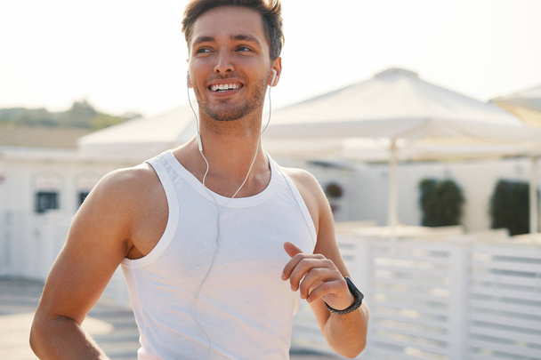 Fitness sportoló futó ember fut egy napsütéses napon, motivációs zene élvezete. Sportos férfi csábító, tökéletes mosoly. Aktív életmód fogalma. - Fotó, kép
