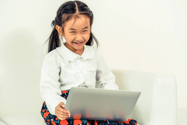 Little happy kid using laptop computer sitting on white sofa. Childhood lifestyle. - Photo, Image
