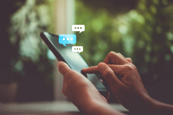 Women hand using smartphone typing, chatting conversation in chat box icons pop up. Social media maketing technology concept.Vintage soft color tone background. - 写真・画像
