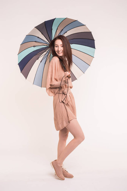 Nuori brunnete aasialainen nainen seisoo värikäs sateenvarjo valkoisella taustalla
 - Valokuva, kuva