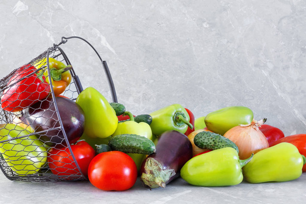 Cosecha de pimiento maduro, tomate, berenjena y cebolla en canasta de metal sobre mesa de piedra
 - Foto, Imagen