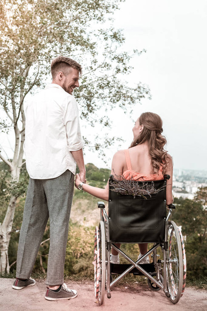 Disabled girl sitting in the wheelchair and holding hands with boyfriend - Foto, imagen