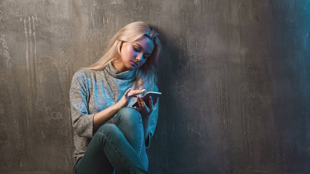 A young woman uses a smartphone, sitting on the floor and looking at the smartphone screen, use the Internet - Foto, Imagem