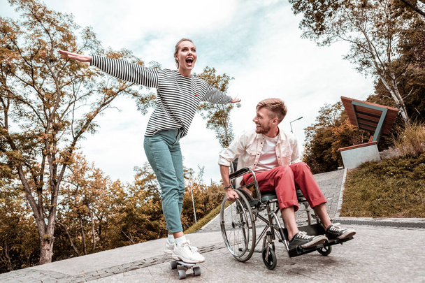 Excited woman standing on penny board and disabled man looking at her - Foto, Imagen
