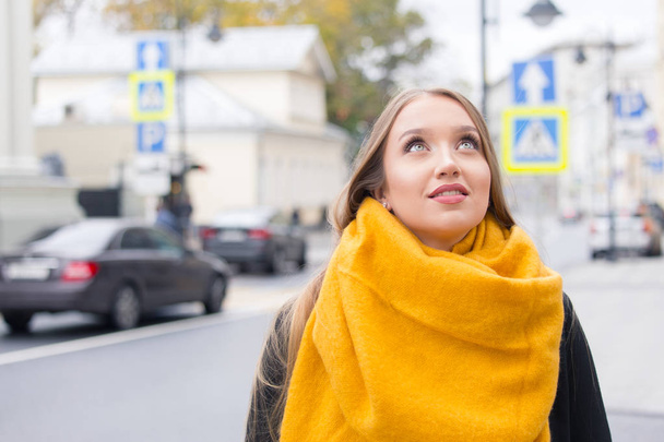 Young girl tourist in the historic center of the city. A blond woman with long hair in a coat and a yellow scarf on an autumn street. - Photo, Image