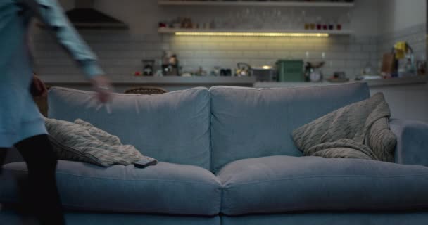 Μια ελκυστική νεαρή γυναίκα κάθεται σε έναν καναπέ σε ένα σκοτεινό δωμάτιο διαβίωσης και διακόπτες στην τηλεόραση. - Πλάνα, βίντεο