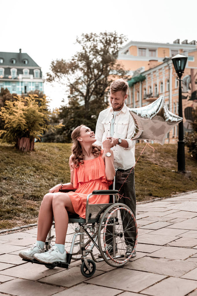 Smiling man holding hand of his disabled girlfriend and looking happy - Fotó, kép