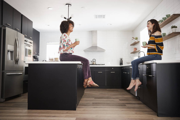 Two Female Friends Meeting For Coffee At Home Sitting On Kitchen Island - Foto, Imagem