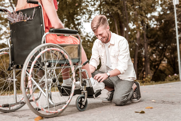 Young man smiling while tying shoelaces of disabled girlfriend - Photo, Image