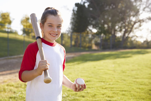 Young girl holding baseball and baseball bat looking at camera - Фото, зображення