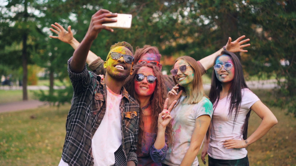 Slow motion van de multi-etnische groep gelukkige studenten met gekleurde vlakken en haar selfie te nemen in het park gebruik van smartphone camera en hebbend pret op Holi festival. - Video