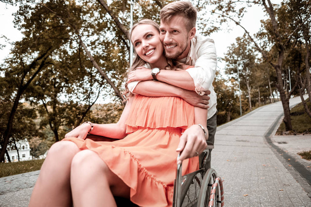 Happy girl sitting in the wheelchair and her boyfriend hugging her shoulders - Foto, imagen