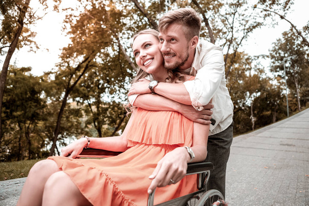 Kind man hugging his disabled girlfriend and looking happy - Photo, image