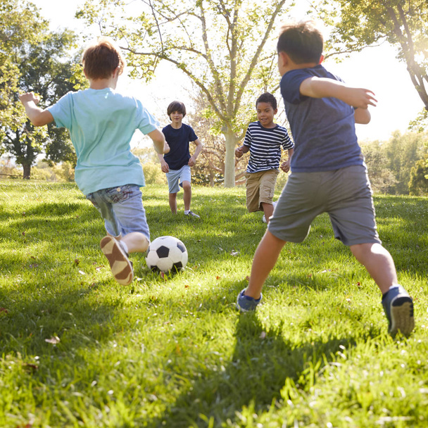 Four schoolboys playing football in park - Foto, imagen