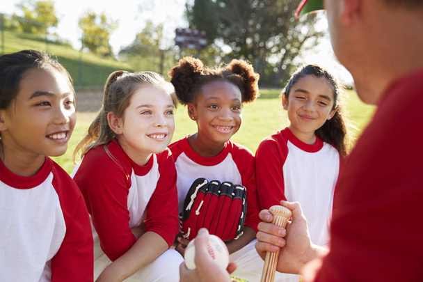 Girl baseball team in team huddle listening to coach - Фото, изображение