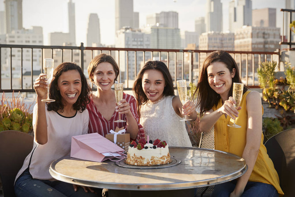Female Friends Making Toast To Celebrate Birthday On Rooftop Terrace With City Skyline In Background - Foto, Imagem
