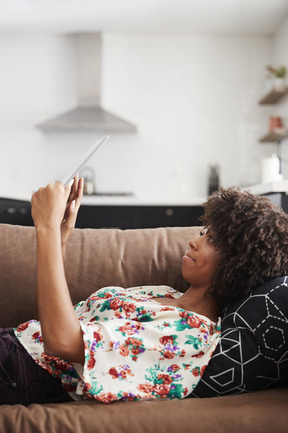 Woman Lying On Sofa At Home Using Digital Tablet - Foto, afbeelding