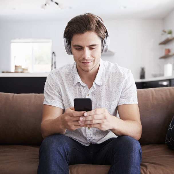 Man Wearing Wireless Headphones Sitting On Sofa At Home Streaming From Mobile Phone - Foto, Bild