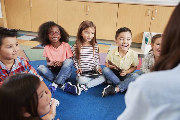 Elementary school kids sitting on floor looking at teacher - Фото, зображення